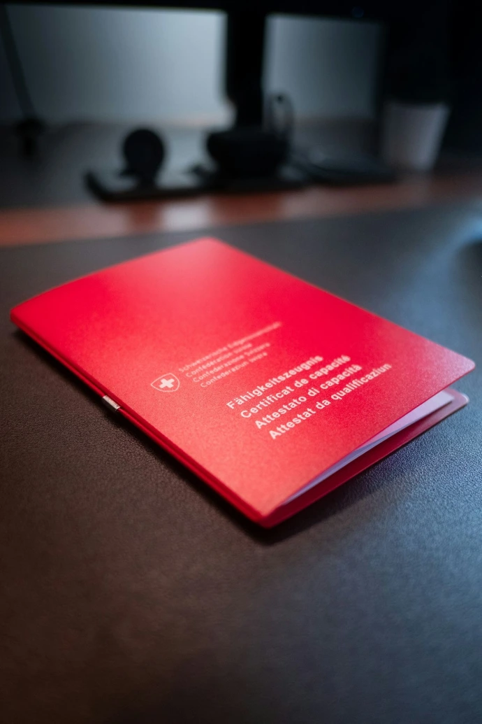 A red swiss certificate of competence on a dark desk.